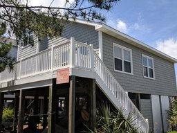 The two story beach house with a front porch that faces the beach.